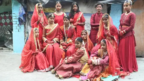 Innovation for Change A group of Indian children participated in a street fashion show. All wear colorful red outfits and ornate jewellery, including maang tikkas, necklaces, earrings and bracelets. 