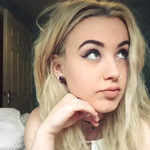 Lauren Redfern A young woman with dyed blonde hair lies on her front on a bed, her chin resting on the back of her right hand. She's looking up and off to the right, a study in posed nonchalance.