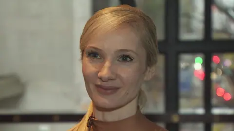 Melissa Hamilton - a woman with long, blonde hair which is tied back in a ponytail is smiling as she looks slightly off camera.