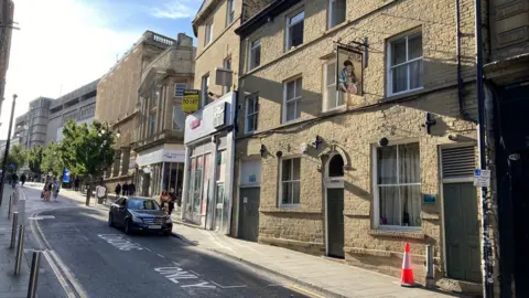 A side view of the sany-coloured, Yorkshire Stone building with the Brutalist-style, concrete Kirkgate Shopping Centre in the background. 