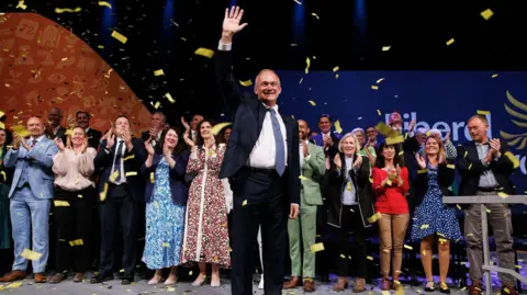  EPA-EFE/REX/Shutterstock Liberal Democrat leader Sir Ed Davey waves after delivering his keynote speech at Liberal Democrat Party Conference in Brighton, with confetti and rows of MPs clapping behind him.