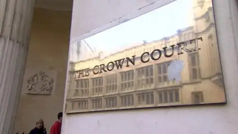 A close up shot of the brass plaque outside Bristol Crown Court that reads The Crown Court. The court's crest is visible in the background.