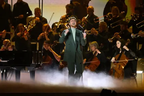 Getty Images Alex Warren performs on stage in an all green suit.