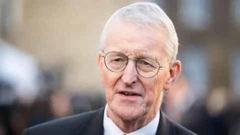 PA Media The head and shoulders of Hilary Benn, wearing thin rimmed glasses and a dark suit with a white shirt.