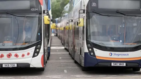 Two Stagecoach branded double decker buses parked side by side, one also decorated with pictures of Remembrance Day poppies.