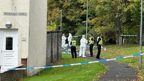 Uniformed police officers and forensic officers in white overalls standing outside a taped-off house on General's Gate.