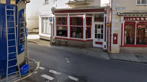 A red and white shop front on a narrow road. There is a small road sign that reads Church Street below the shop window. 