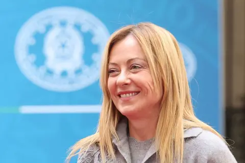 Getty Images Italian Prime Minister Giorgia Meloni smiling in front of a blue background