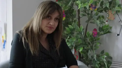 Dali Kaur sits in a chair and looks forwards. She wears a dark coloured blouse.