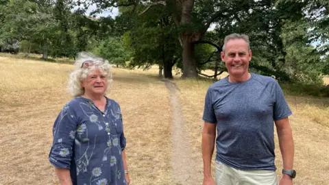 LDRS Parker is stood in a floral blue top with Tom Wood. The pair are stood on a footpath with two trees in the background.
