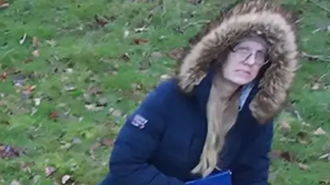 Warwickshire Police A CCTV screenshot of a woman walking an animal in a park. She is wearing a blue puffer jacket and has the hood up 