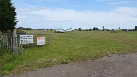 Clacton airfield on a clear day. The airfield has a number of light aircraft positioned on its grass surface.