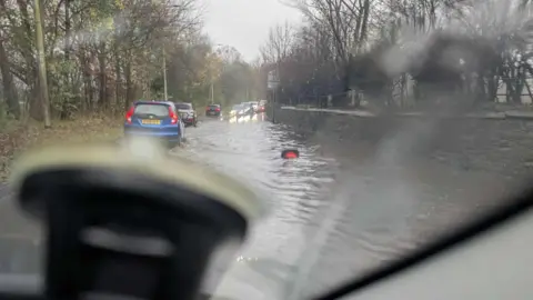 Kate Inchbold-Stevens A picture taken from inside a car looking out at a line of cars driving on the extreme left-hand side of the road to escape the road surface flooding in Great Corby. 