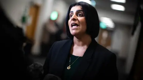 PA Media Shabana Mahmood speaks into press microphones in a hallway