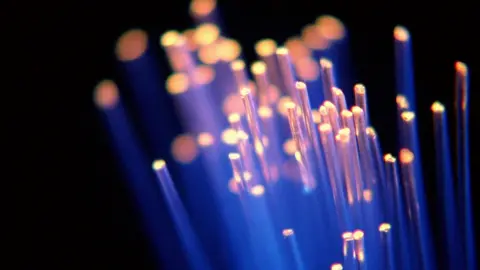 Getty Images Strands of blue fibre optic cable light up in the dark with their ends shining with an orange glow