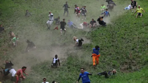 People compete in the annual Cooper's Hill Cheese-Rolling and Wake competition near Brockworth. A number of men are running down the steep grass hill. 