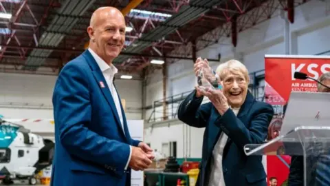 KSS Air Ambulance KSS founder Kate Chivers lifts a glass trophy - her lifetime achievement award - and smiles at the camera alongside chief executive David Welch