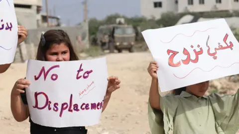 Palestinian children hold up posters saying "No to displacement" in English and Arabic at a protest near Nur Shams refugee camp, near Tulkarm, in the occupied West Bank