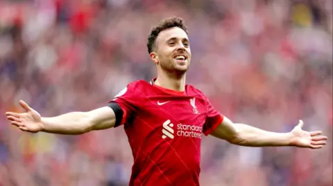 PA Media Diogo Jota, wearing a red Liverpool shirt, smiles with both arms extended after scoring a goal