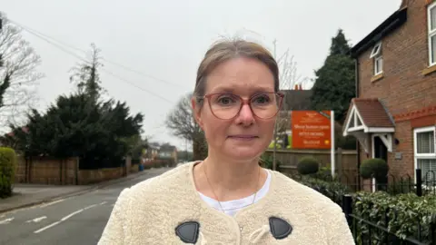 Rebecca is wearing a cream white fleece and is behind a road.