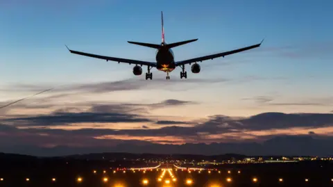 Getty Images A plane about to land on a runway as the sun sets