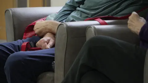 Shaun Whitmore/BBC Care home residents sitting in chairs. Their hands, legs and lower torsos are visible.