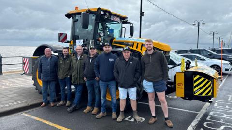 A group of farmers in front of the tractor the used to drive around the British coastline