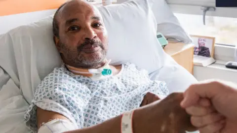 RCSLT The picture shows a person resting while fist pumping another individual recovering from surgery to his throat. 