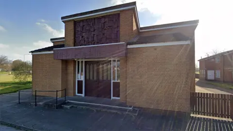 The exterior of St Mary Queen of Martyrs in Bransholme a single-storey building built of light bricks with dark decoration panels above the doors.