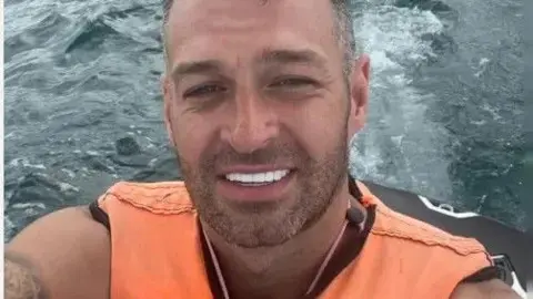North Yorkshire Police A man with short hair and beard and white teeth on the back of a jet ski wearing an orange life jacket
