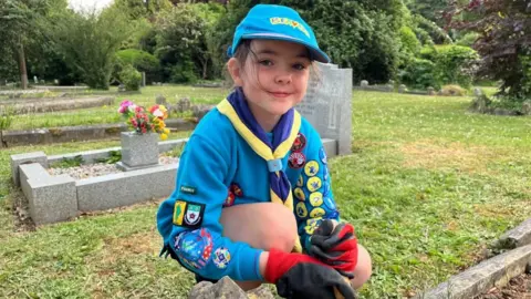 Girl in blue jumper crouched down next to a grave