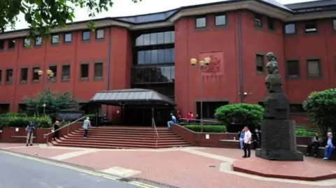 BBC The exterior of a large red brick building with dark windows and steps leading up to a large entrance