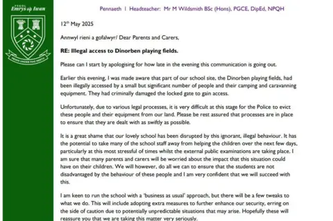 Ysgol Emrys Ap Iwan A copy of the letter to parents from the head teacher. On the left there is a green indent and the text is then formatted on the right.
In black font the letter states:
Dear Parents and Carers,
RE: Illegal access to Dinorben playing fields.
Please can I start by apologising for how late in the evening this communication is going out.
Earlier this evening, I was made aware that part of our school site, the Dinorben playing fields, had been illegally accessed by a small but significant number of people and their camping and caravanning equipment. They had criminally damaged the locked gate to gain access.
Unfortunately, due to various legal processes, it is very difficult at this stage for the Police to evict these people and their equipment from our land. Please be rest assured that processes are in place to ensure that they are dealt with as swiftly as possible.
It is a great shame that our lovely school has been disrupted by this ignorant, illegal behaviour. It has the potential to take many of the school staff away from helping the children over the next few days, particularly at this most stressful of times whilst the external public examinations are taking place. I am sure that many parents and carers will be worried about the impact that this situation could have on their children. We will however, do all we can to ensure that the students are not disadvantaged by the behaviour of these people and I am very confident that we will succeed with this.
I am keen to run the school with a 'business as usual' approach, but there will be a few tweaks to what we do. This will include adopting extra measures to further enhance our security, erring on the side of caution due to potentially unpredictable situations that may arise. Hopefully these will reassure you that we are taking this matter very seriously.