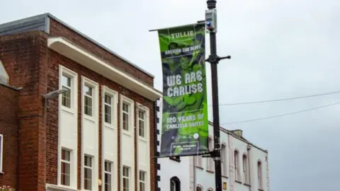 Tullie A green and blue flag on a lamp post which reads We are Carlise
