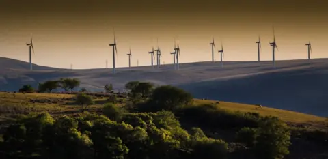 Getty Images Wind farm on a hill at sunset or sunrise