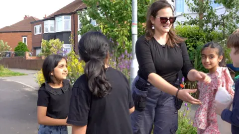 Oli Constable/BBC A woman hands out water to children