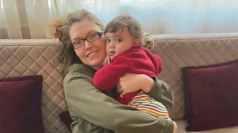 Catherine Flanagan Catherine Flanagan with her son David. She is wearing glasses and a green jumper. David, wearing a red cardigan, hugs his mother and looks at the camera. 