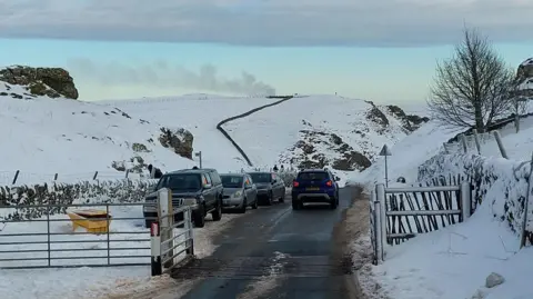 Three parked cars along a snowy stretch of road with one driving past