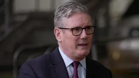 Sir Keir Starmer being interviewed by the BBC. He is wearing glasses, a navy suit and purple tie.