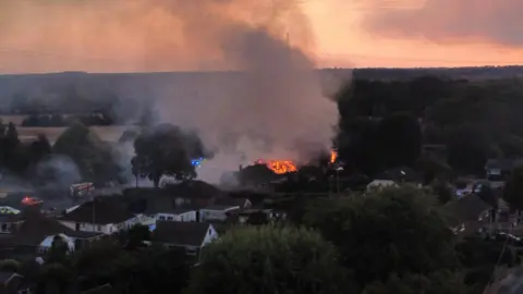 Orange flames consume the roofs of two properties with smoke trailing into the sky in an aerial shot.