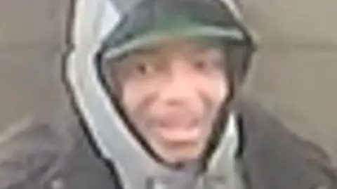 A grainy CCTV still of a young man in a grey hoodie.