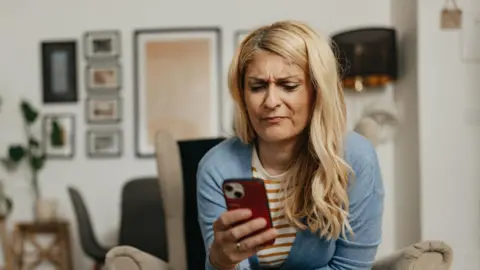 Blonde woman looks frustrated while using her smartphone at home