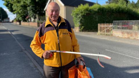 Man in orange fleece holding a litter-picker and three carrier bags