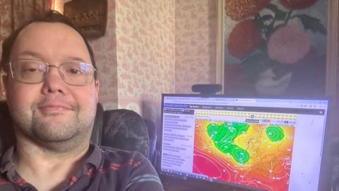 Gavin smiling in front of computer with weather map