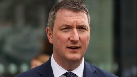 PA Media A close up of John Finucane in a dark blue suit, white shirt and black and white tie
