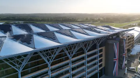 A bird's eye view of Ascot Racecourse's Grandstand, with two long Union flags pitched at its entrance.