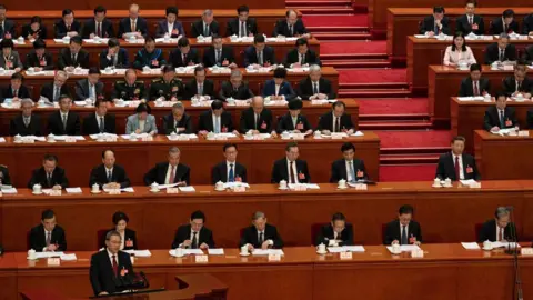 Getty Images Chinese Premier Li Qiang, bottom left, speaks at the podium as President Xi Jinping, centre right, and other senior government members look on at the 2024 session of the National Peoples Congress