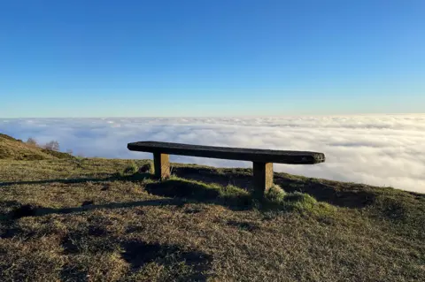 Nathan VG / BBC Weather Watchers Malvern mist with a bench near the top of a hill and lots of cloudy white mist visible beyond.