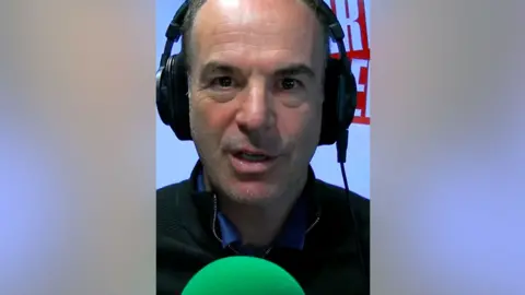 Martin Lewis, a man with over-ear headphones on and a green microphone.