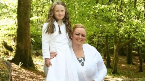 Donna Harper Shows a young girl on the left and a woman on the right, both dressed in white, in a wooded area